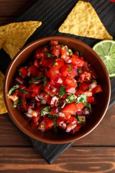 a bowl full of salsa with tortilla chips and lime wedges on the side