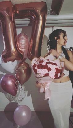 a woman holding a bouquet of roses in front of balloons and the number twenty sign