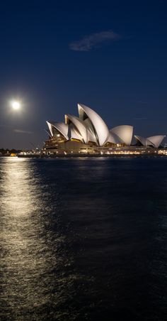 the sydney opera house is lit up at night with full moon in the sky above it