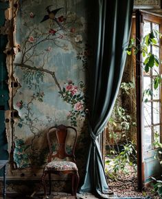 a chair sitting in front of a window next to a wall with flowers on it