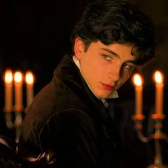 a young man sitting in front of some candles wearing a black suit and white shirt