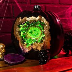 a halloween pumpkin decorated with green and gold glitters on a wooden table next to other decorations