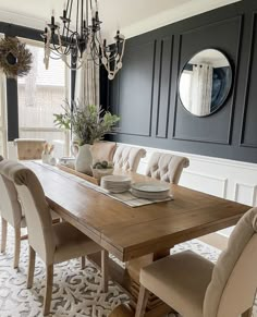 a dining room table with chairs and a mirror on the wall above it, in front of a chandelier