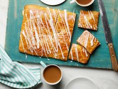 some food is laying out on a cutting board next to two cups of coffee and a knife