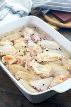 a white casserole dish filled with chicken and carrots on a wooden table