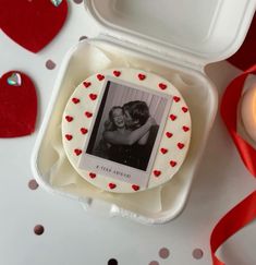 a cake in a white box with red hearts on it and a candle next to it