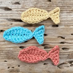 three crocheted bows are sitting on a wooden surface, one is blue and the other is pink