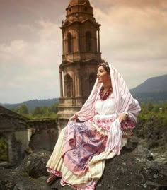 a woman sitting on top of a large rock next to a church steeple in the background