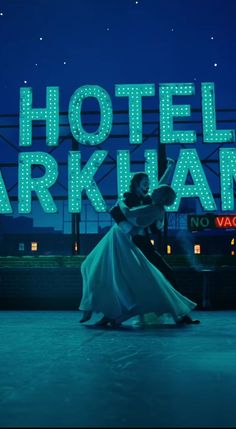 a man and woman dance in front of the hotel arkland sign at night time