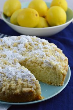 a lemon cake with powdered sugar sits on a plate next to a bowl of lemons