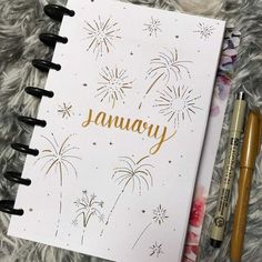 an open notebook with the word january written in gold on it next to two pens