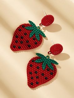 two red strawberries are hanging from the back of some earrings on a white surface