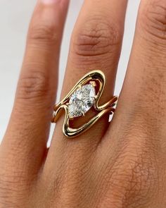 a woman's hand wearing a gold ring with a diamond in the middle and an open band around it