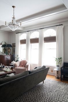 a living room filled with furniture and a chandelier hanging from the ceiling next to two windows