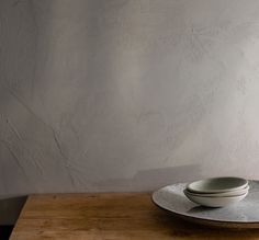 a bowl and plate on a wooden table in front of a white wall with peeling paint