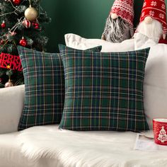 two christmas pillows sitting on top of a white couch next to a christmas tree and other decorations