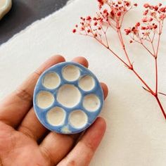 a person holding a blue and white object in their hand next to some red flowers