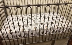 a crib with a white sheet and black iron bars on the sides, next to a wooden floor