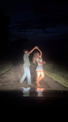 two people dancing in the dark on a street at night with their arms around each other