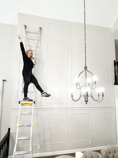 a woman is standing on a ladder in the middle of a room with white walls