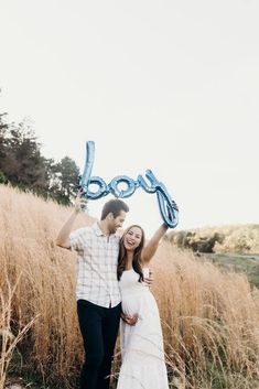 a man and woman standing in tall grass holding up balloons that say boodoo