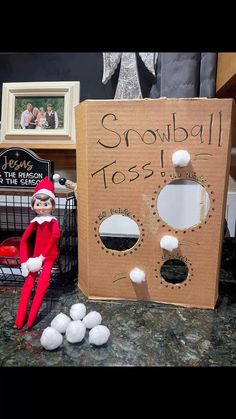 an elf is sitting in front of a cardboard box that says snowball toss