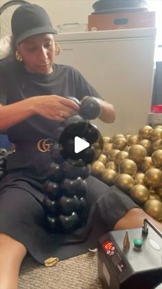 a woman sitting on the floor in front of gold balls and holding an object with one hand