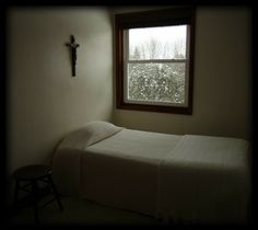 a bed sitting under a window next to a cross on the side of a wall