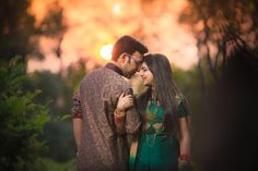 a man and woman standing next to each other in front of some trees at sunset