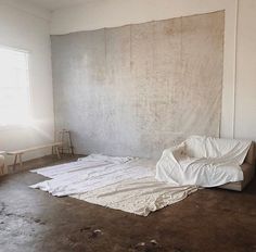 an empty room with white sheets on the floor and a large piece of cloth covering the wall