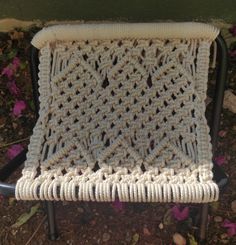 a white crocheted chair cushion sitting on top of a black metal chair with purple flowers in the background