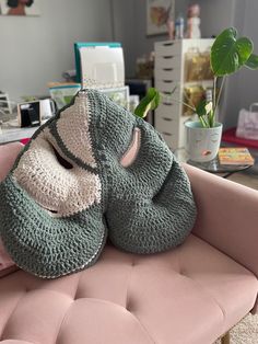 two crocheted baby shoes sitting on top of a pink chair next to a potted plant