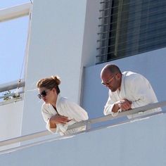 a man and woman standing next to each other on a balcony looking at something in the distance