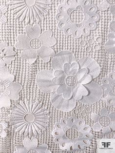 the back side of a white lace fabric with flowers and leaves on it's edges