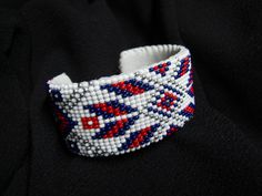 a beaded bracelet with red, white and blue beads on black fabric background in close up view