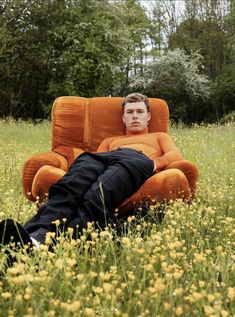 a man laying on top of an orange chair in a field