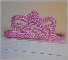 a pink crocheted crown sitting on top of a white shelf next to a wall