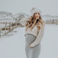 a pregnant woman standing in the snow with her hands on her head and wearing a hat