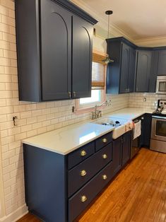 a kitchen with dark blue cabinets and white counter tops, wood flooring and stainless steel appliances