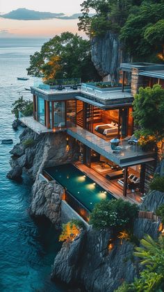 an aerial view of a house on the edge of a cliff by the ocean at dusk