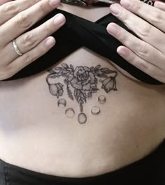 a woman's stomach with a flower tattoo on her belly and two hands holding it