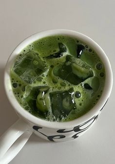 a cup filled with green liquid sitting on top of a white table next to a spoon