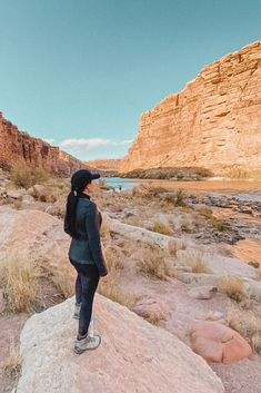 a woman standing on top of a rock next to a river