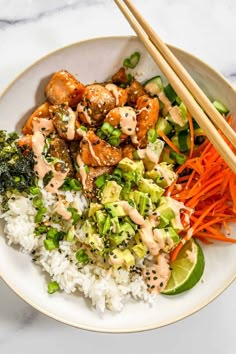 a white plate topped with rice, broccoli and carrots next to chopsticks