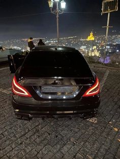 the back end of a black car parked on a cobblestone road at night