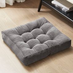 a grey square dog bed sitting on top of a hard wood floor next to a white rug