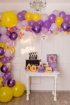 a birthday party with purple and yellow balloons on the wall, cake table and decorations