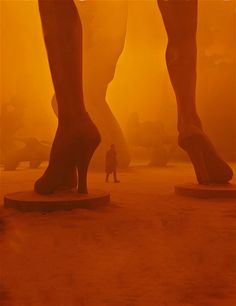 a person standing in front of two large feet on pedestals with orange fog behind them