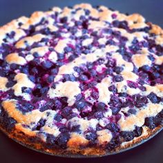 a pie with blueberries and cream on it sitting on a black tablecloth covered surface