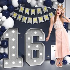 a woman wearing a tiara standing in front of balloons and garlands with the number sixteen on it